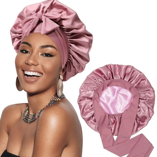 Woman wearing a pink satin hair bonnet with bow for frizz control, product shown on white background